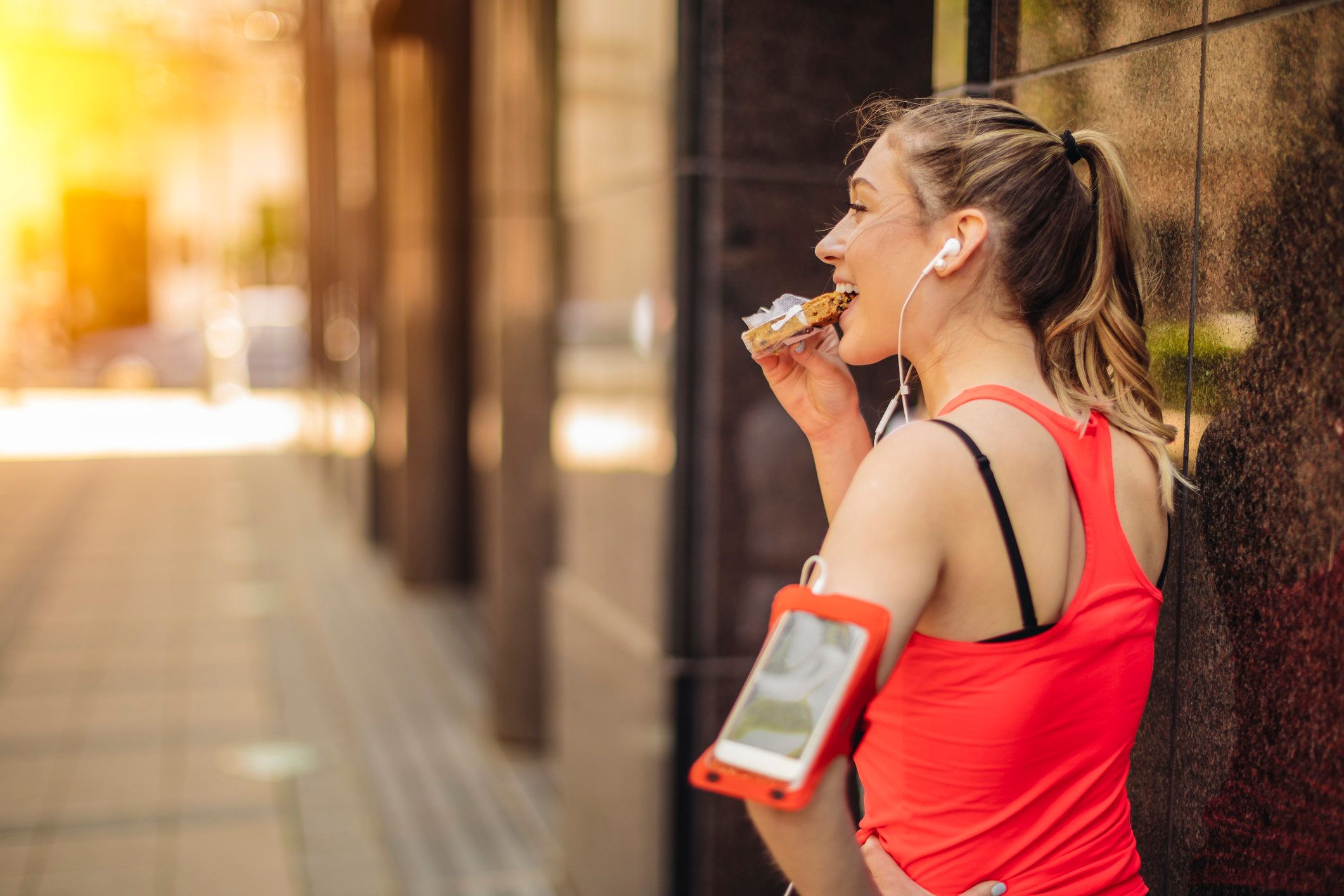 woman stops on street after workout and eats a healthy snack, looks happy