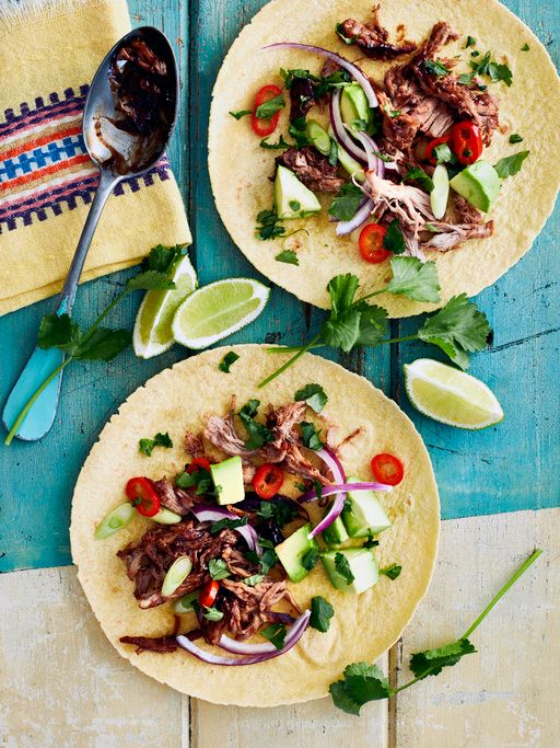 2 open-faced tacos with meats, red onion, tomato and lime on a blue table
