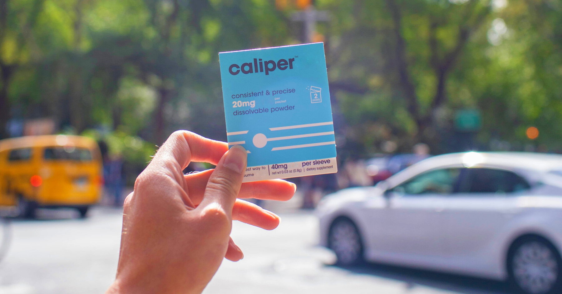 hand holds a blue package that says "caliper' in front of a blurred city street